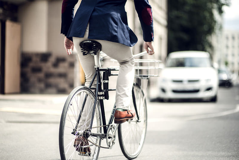 Мужчина в белых брюках и синем пиджаке на велосипеде